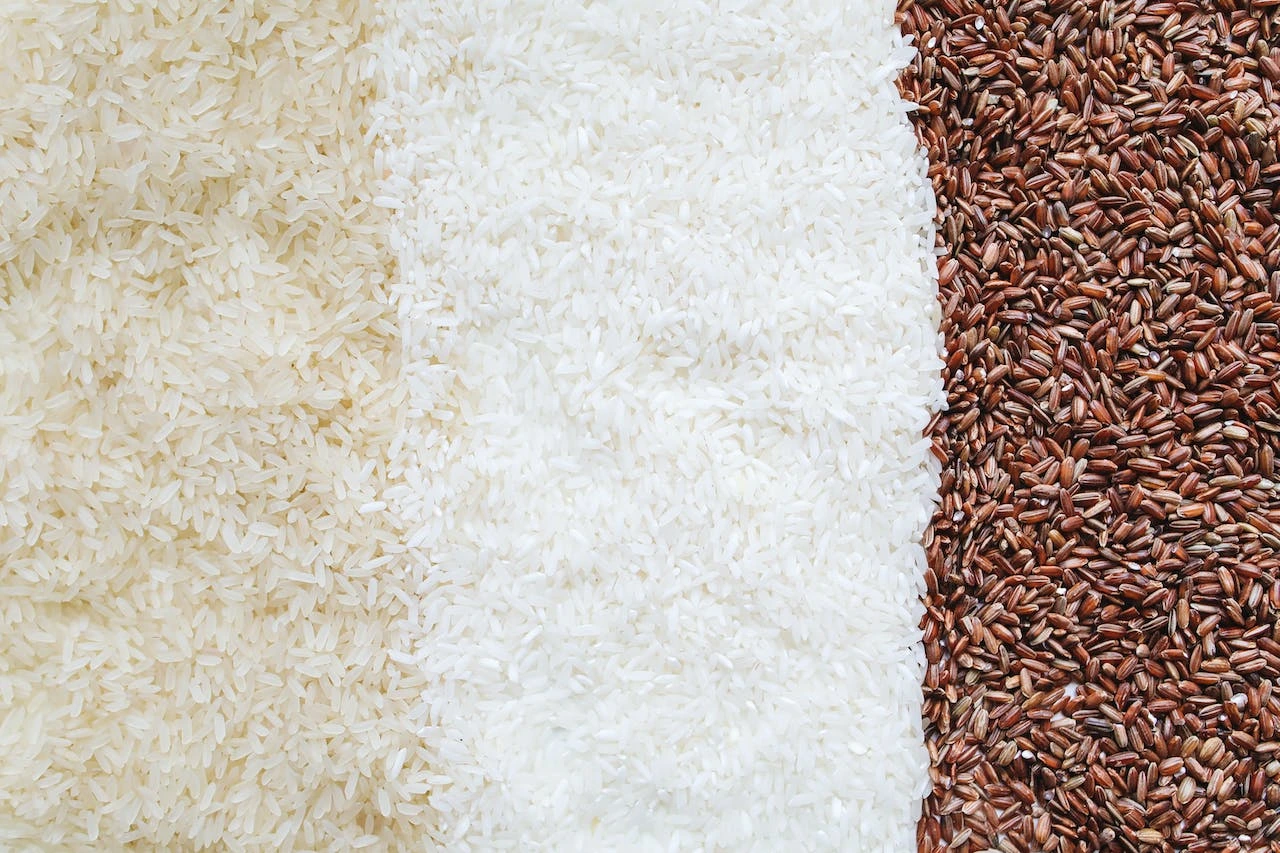 Three varieties of rice grains: white long-grain, jasmine, and brown red rice