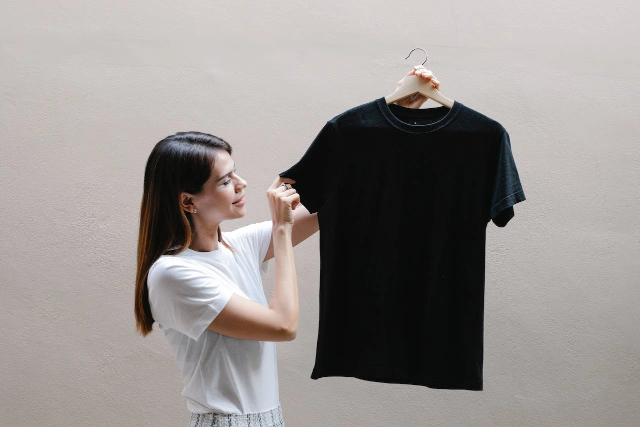 Woman in white shirt holding black t-shirt on wooden hanger
