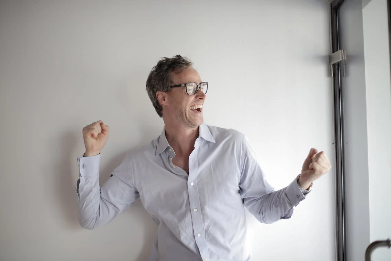 Excited professional in glasses celebrates with fist pump against white wall