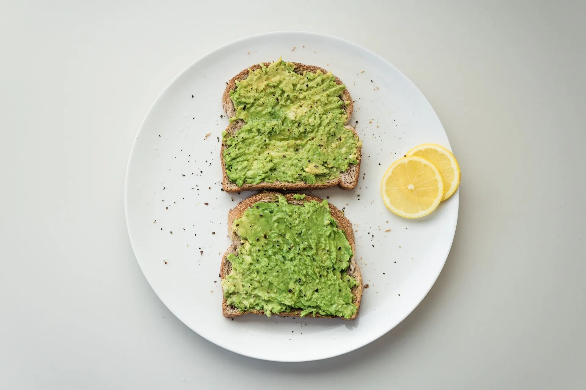 Avocado toast with lemon slices on a white plate
