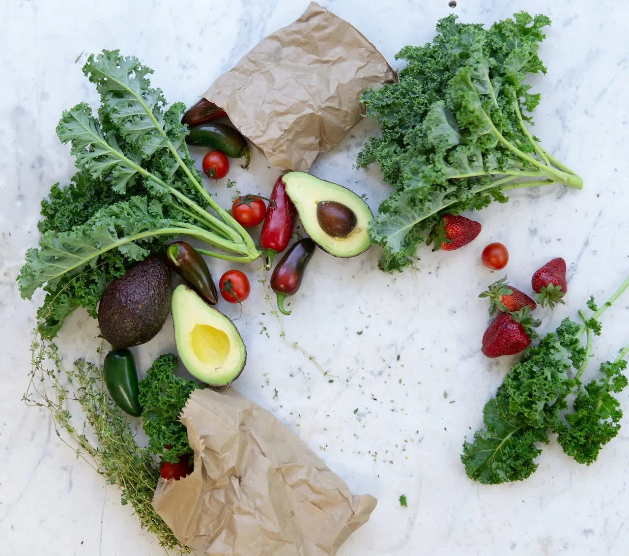 Fresh kale, avocados, strawberries, peppers, and tomatoes on marble surface