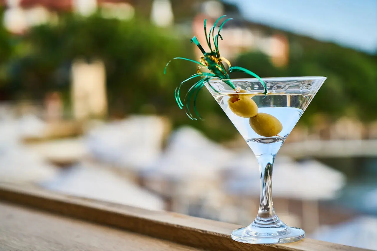 Martini cocktail with olives and garnish on blurred resort background