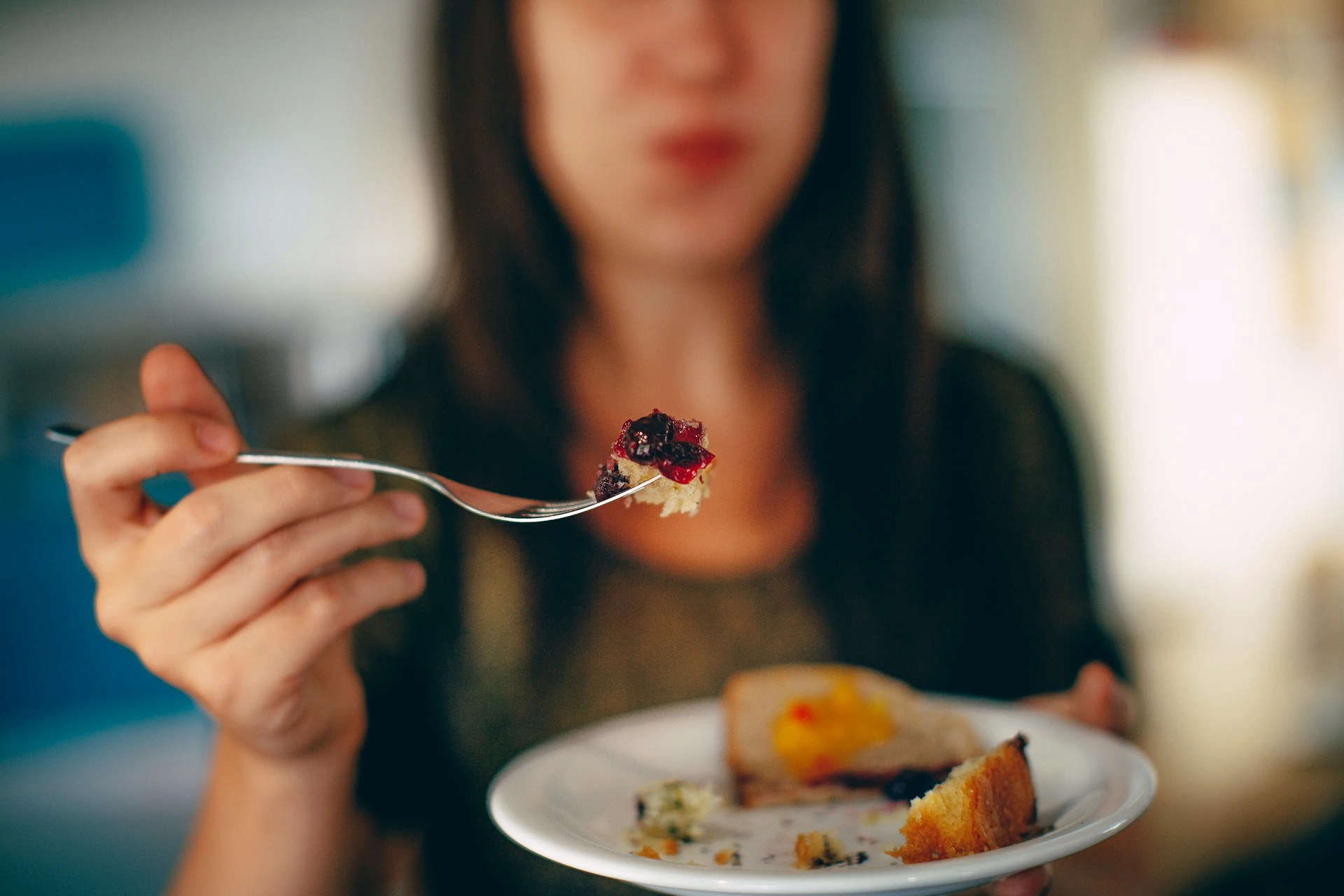 Woman holding fork with red berries over plate of food