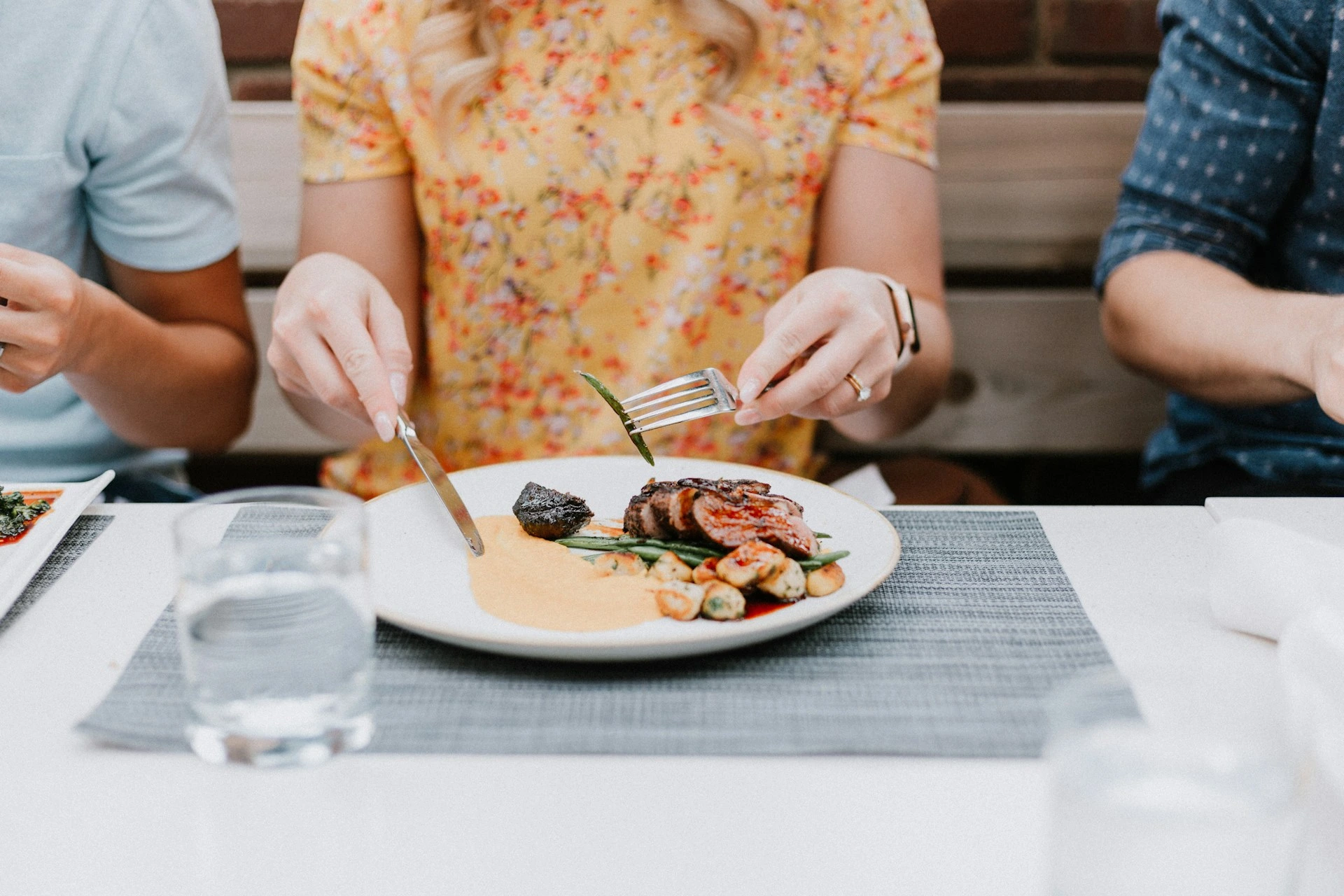 Person eating gourmet plated meat and vegetable dish with fork at restaurant table