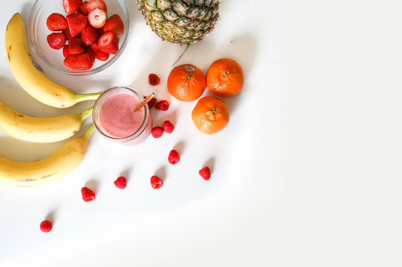Overhead view of fresh fruits and smoothie: bananas, strawberries, raspberries, oranges, and pineapple.