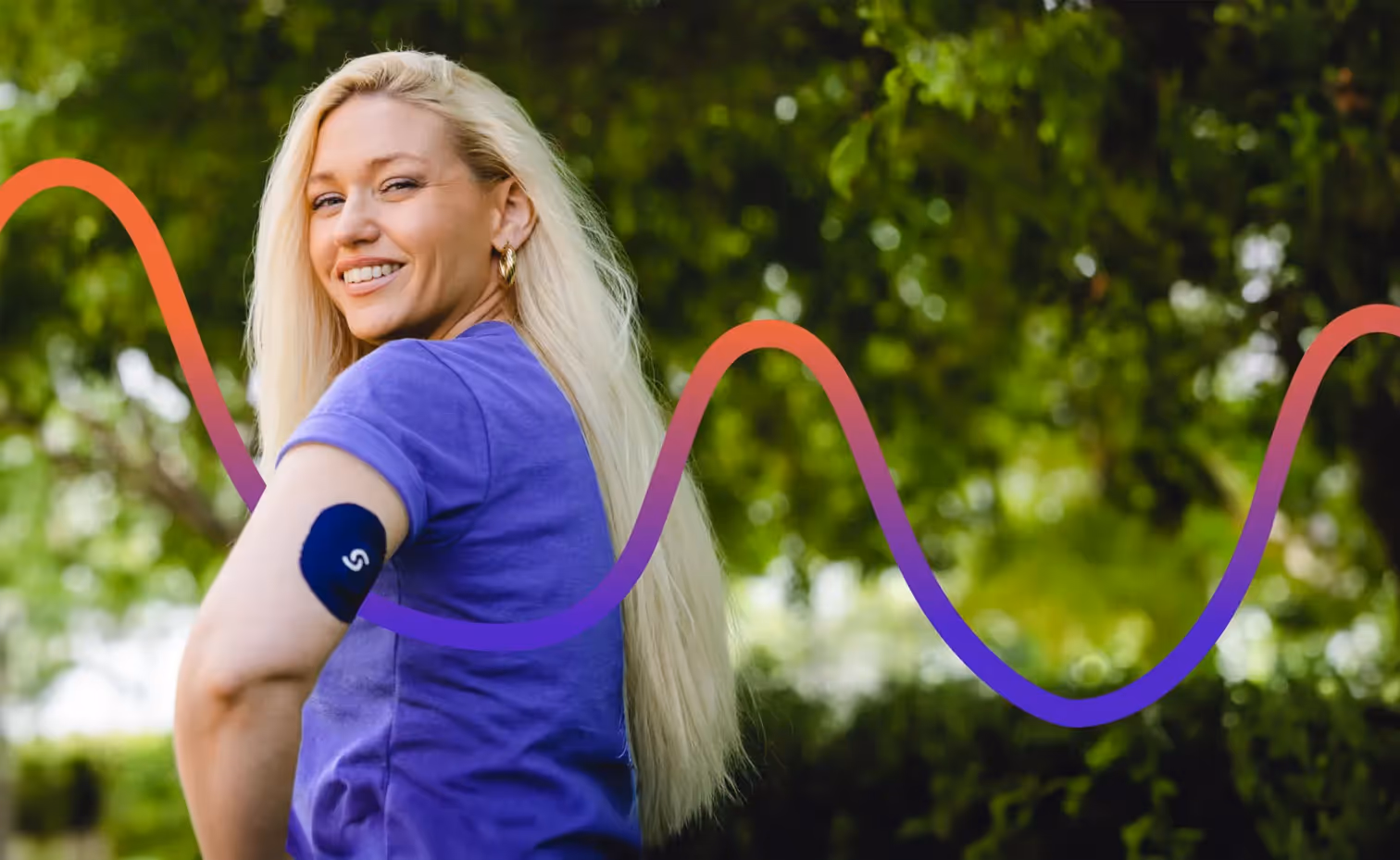 Smiling woman in blue shirt with continuous glucose monitor outdoors