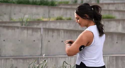 Athlete checking fitness tracker by concrete wall with plants