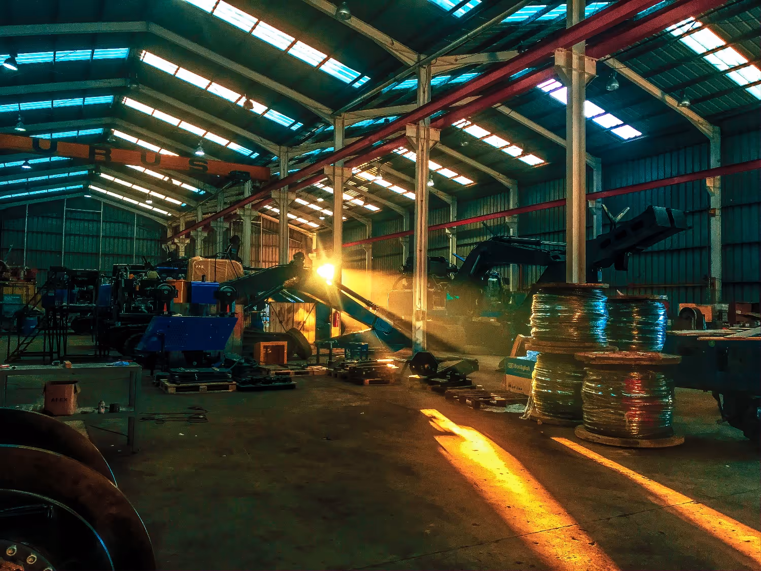 Sunlight streams through warehouse windows onto industrial machinery and large spools inside the building.