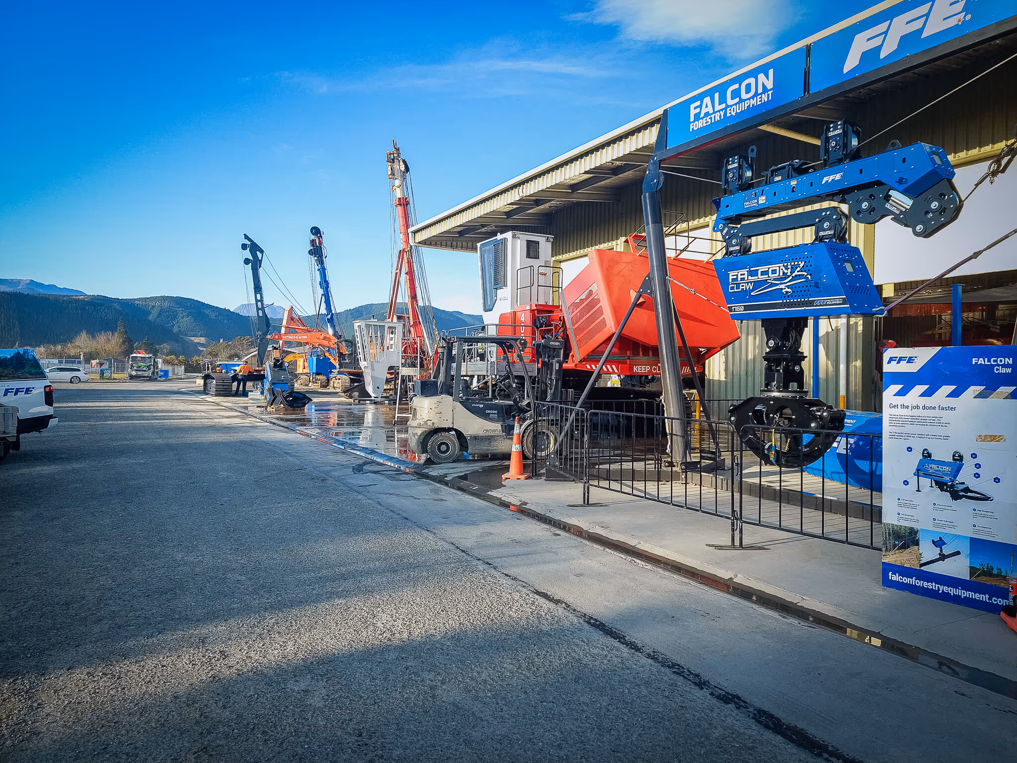 Outdoor display of forestry equipment and machinery under a clear blue sky with mountains in the background.