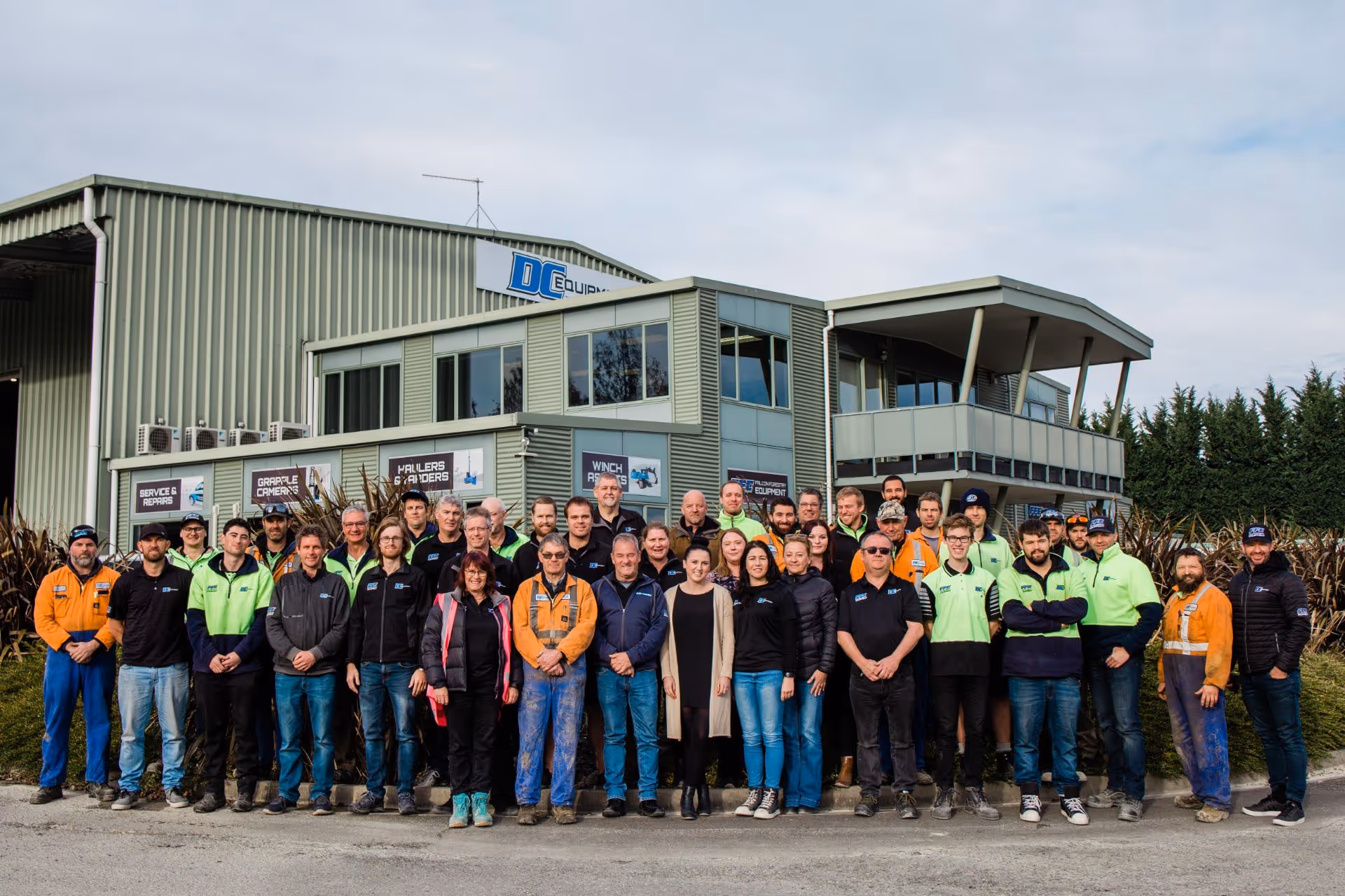 A large group of diverse men and women standing in front of an industrial building with a DC Equipment sign.
