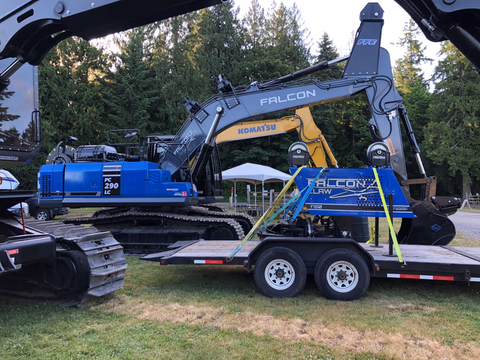 Blue Komatsu PC 290 LC excavator with Falcon logging equipment on a trailer in a park setting.