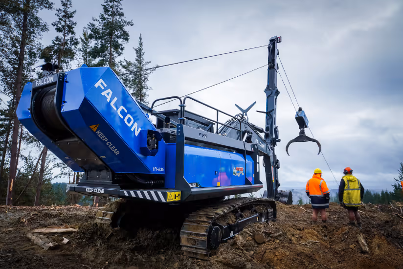 Blue Falcon excavator with grapple arm and two workers in orange and yellow jackets on dirt site.