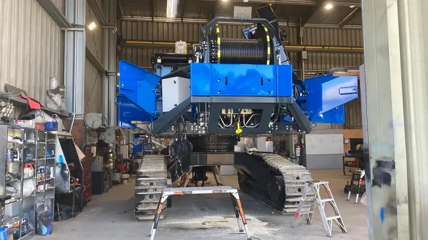 Large blue heavy machinery with tracks inside a warehouse or workshop area.
