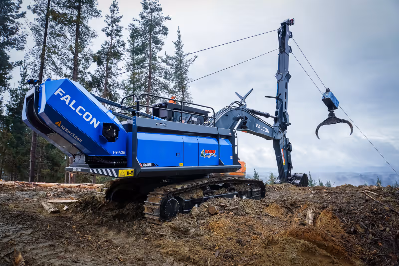 Large blue Falcon forestry machine with claw attachment working on muddy forest ground.