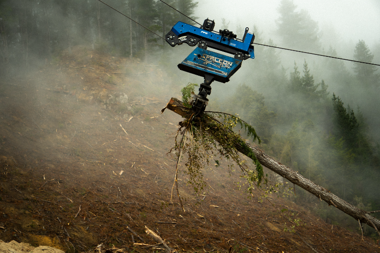 Blue rescue robot using cable to lift fallen tree on foggy, cleared forest slope.