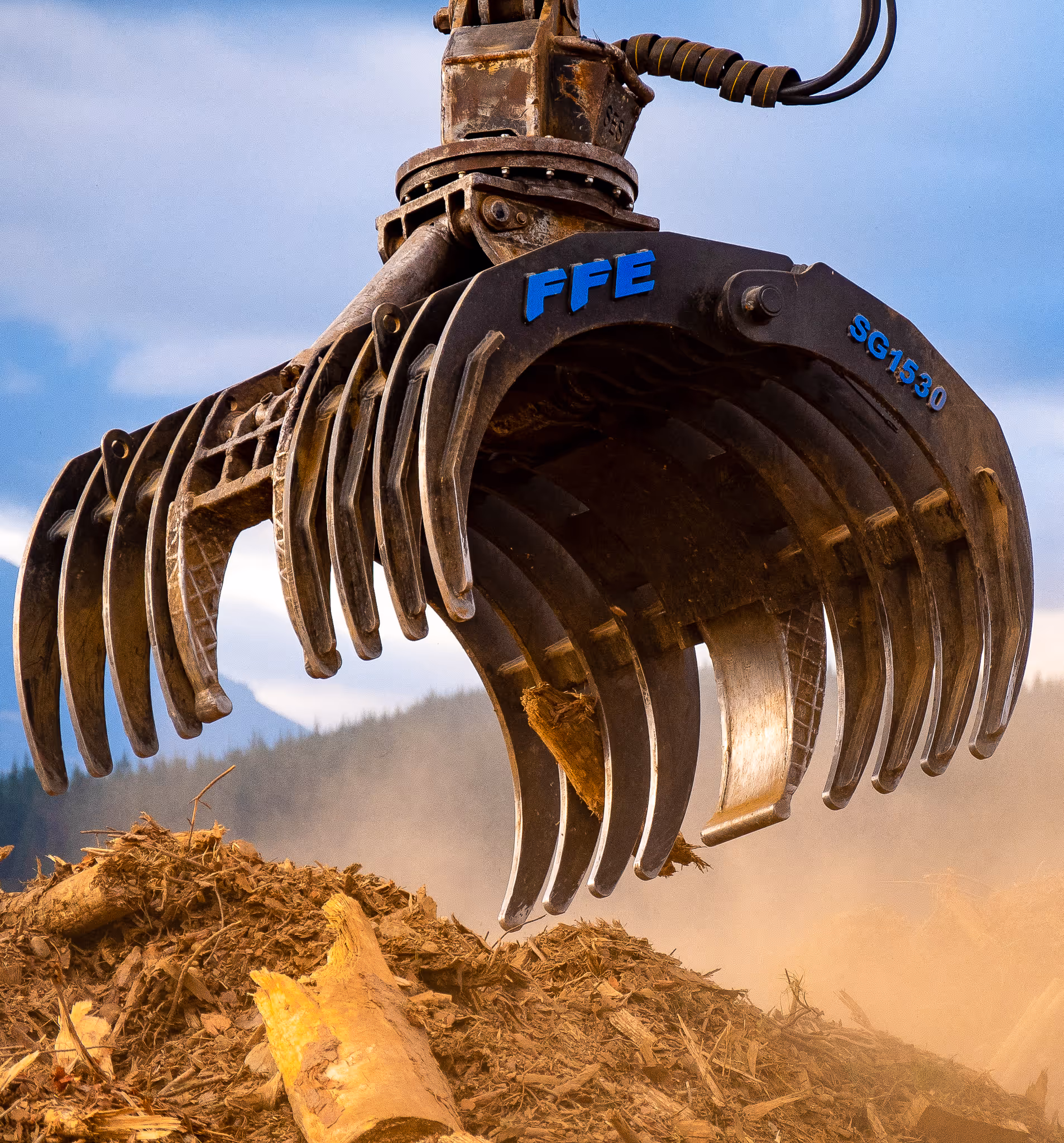 Close-up of heavy-duty mechanical claw labeled FFE SG1530 grabbing wood debris on a dusty site.