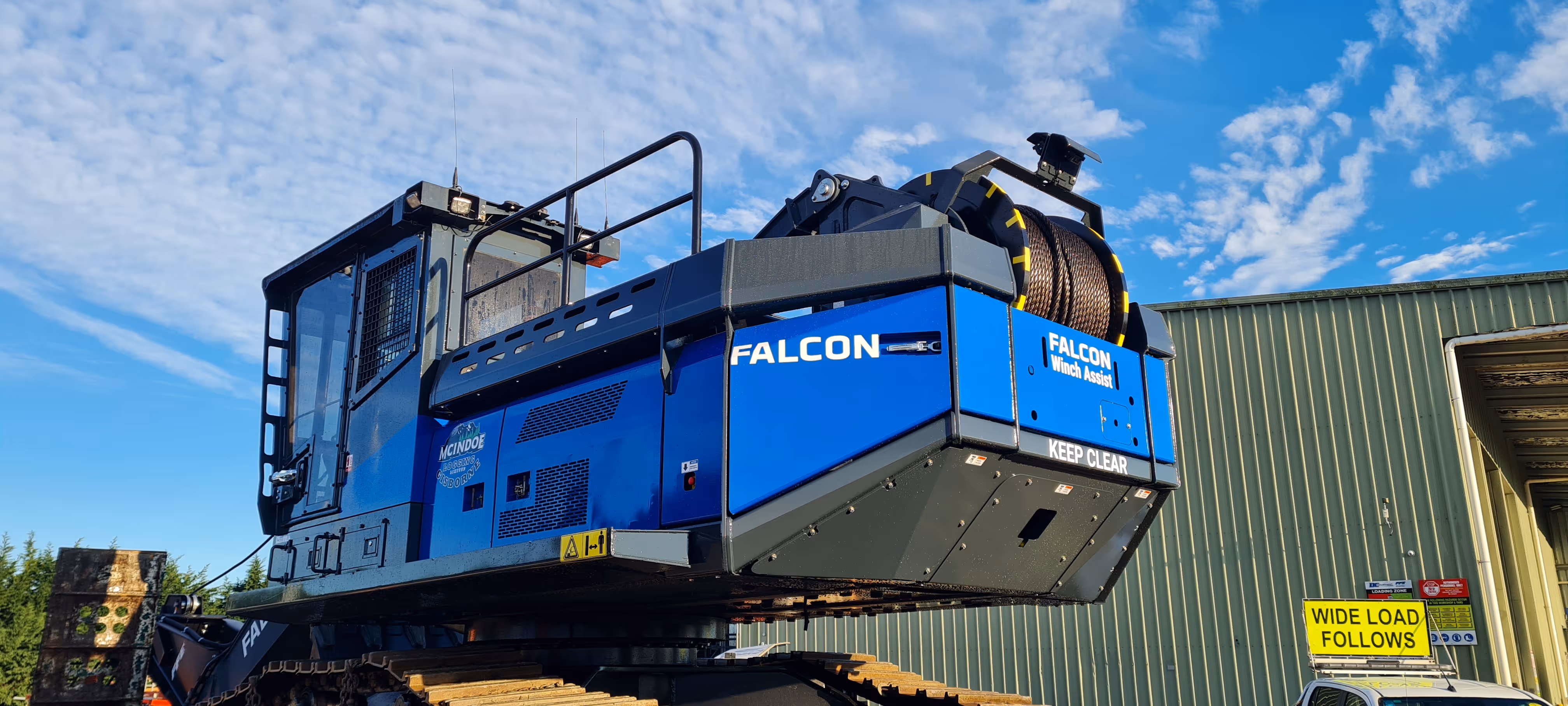 Blue and black Falcon heavy construction winch machine parked near industrial building.