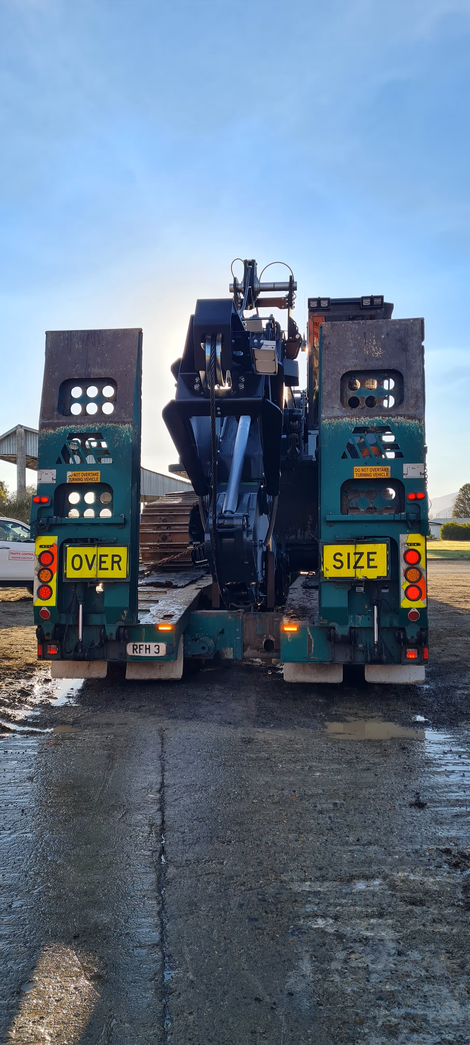Rear view of heavy machinery loaded on a trailer with 'OVER SIZE' signs on each side.