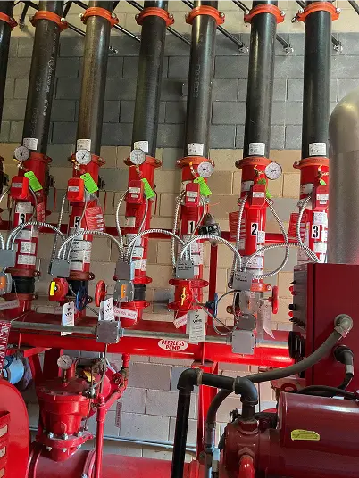 Red industrial piping system with vertical black pipes, pressure gauges, valves, and control devices in a utility room.