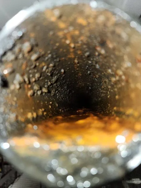 Worker in a yellow hard hat and reflective vest using a flashlight to check a pressure gauge on red industrial pipes.
