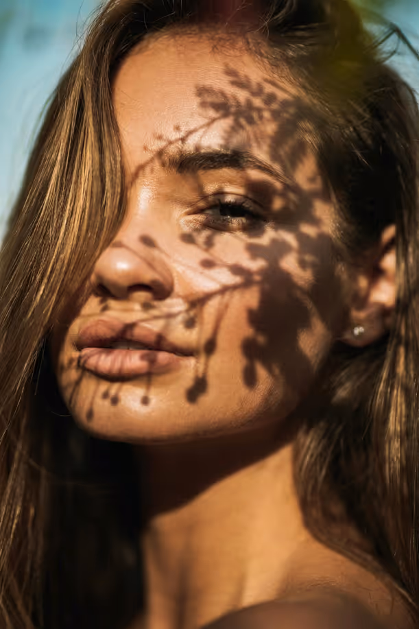 Close-up of a woman's face with shadows of branches and berries cast across her skin.