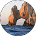 Natural rock arch over the ocean with waves crashing beneath at sunset.