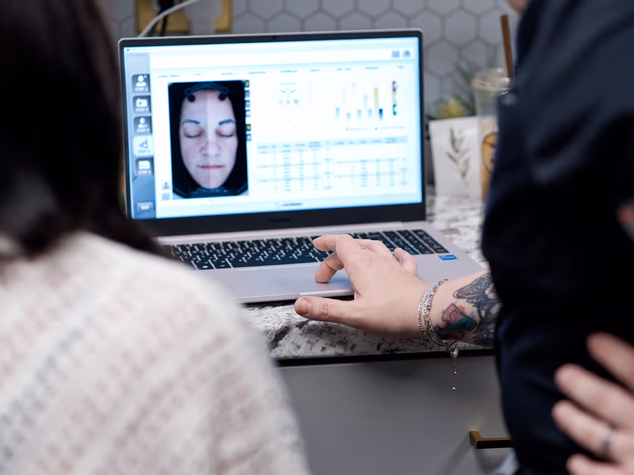 Person with a tattooed arm operating a laptop showing a facial scan analysis with a close-up of a closed-eyed face and data charts.