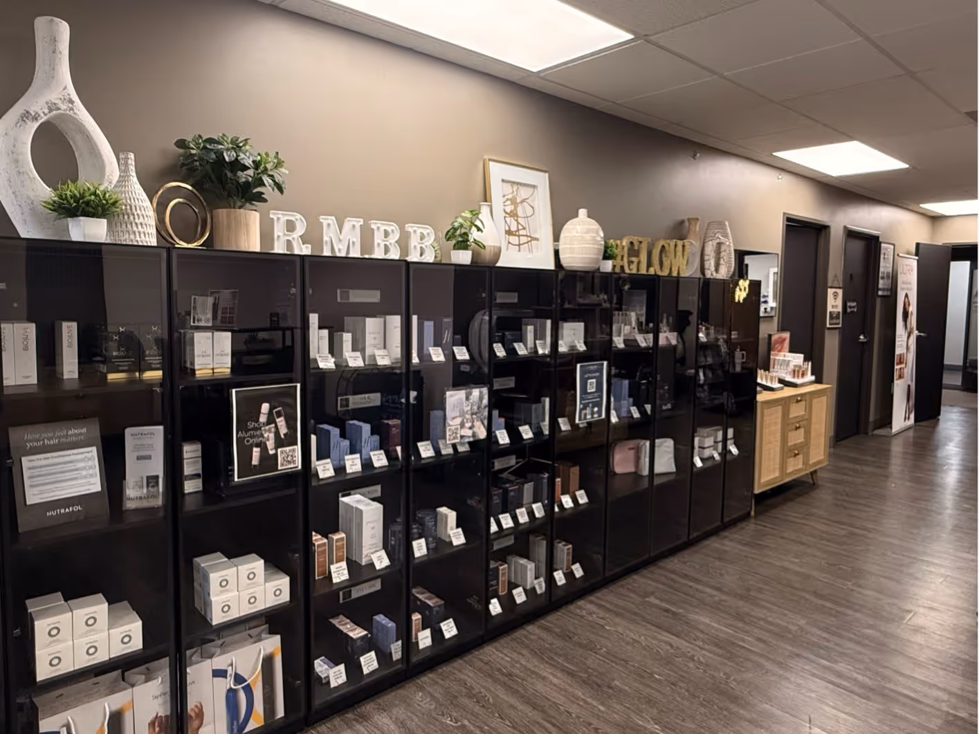 Interior view of a skincare and cosmetic shop with black glass display cabinets filled with various beauty products and decorative plants on top.
