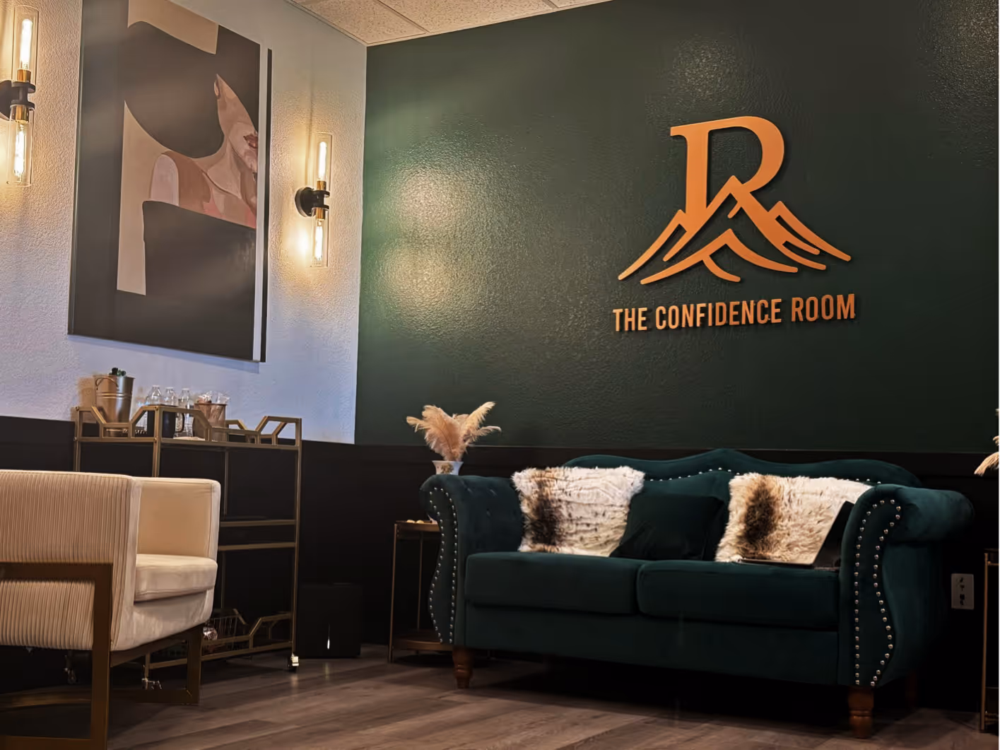 Modern waiting area with dark green couch, light beige armchair, and wall sign 'The Confidence Room' in gold letters.