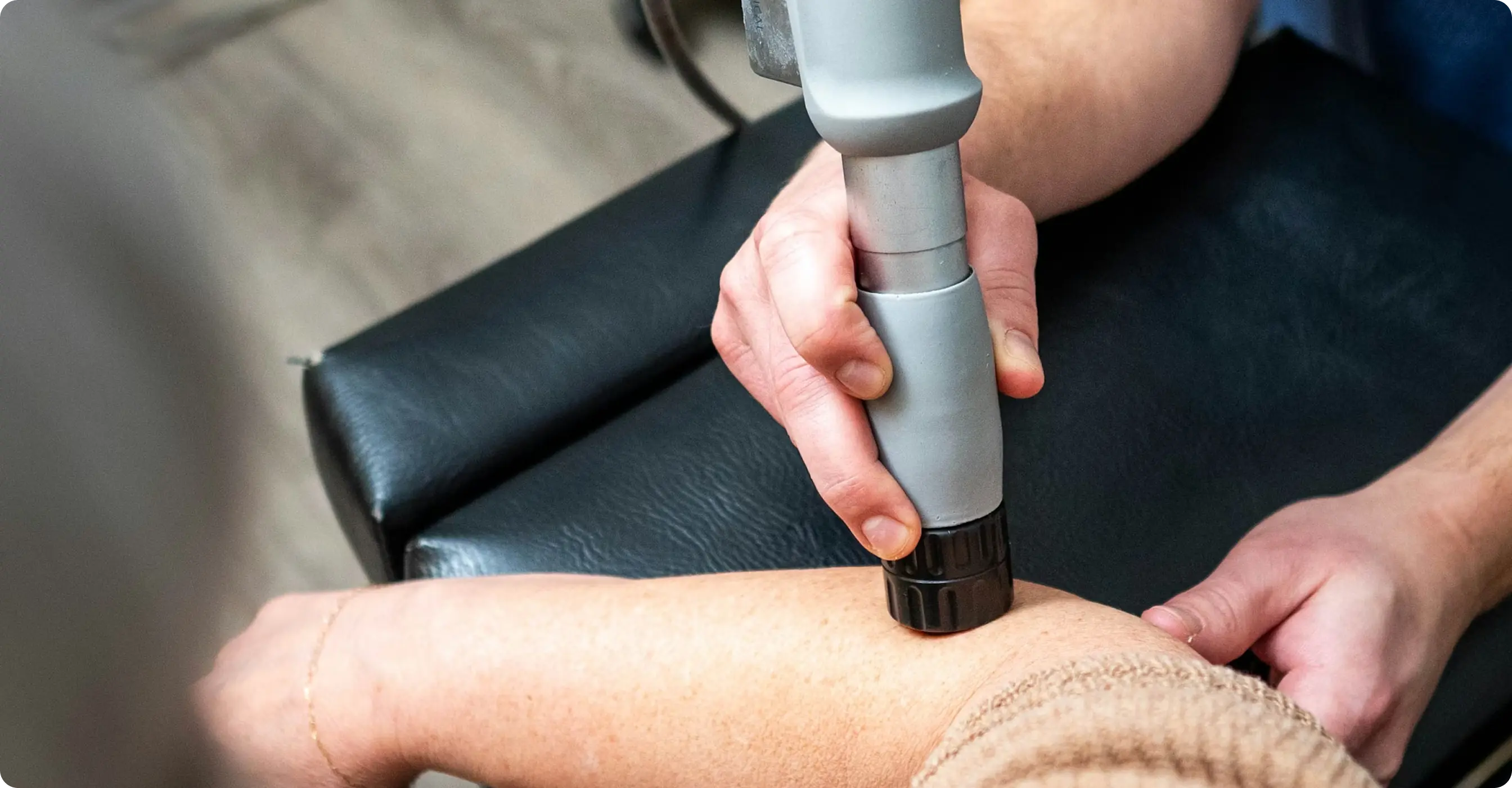 Physiotherapy treatment using a handheld shockwave device on a patient's forearm.