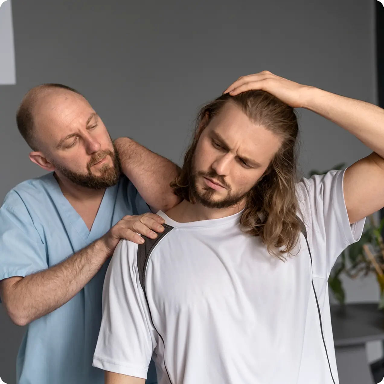 Healthcare professional in scrubs examining a man’s neck while the man stretches his neck and holds his head.