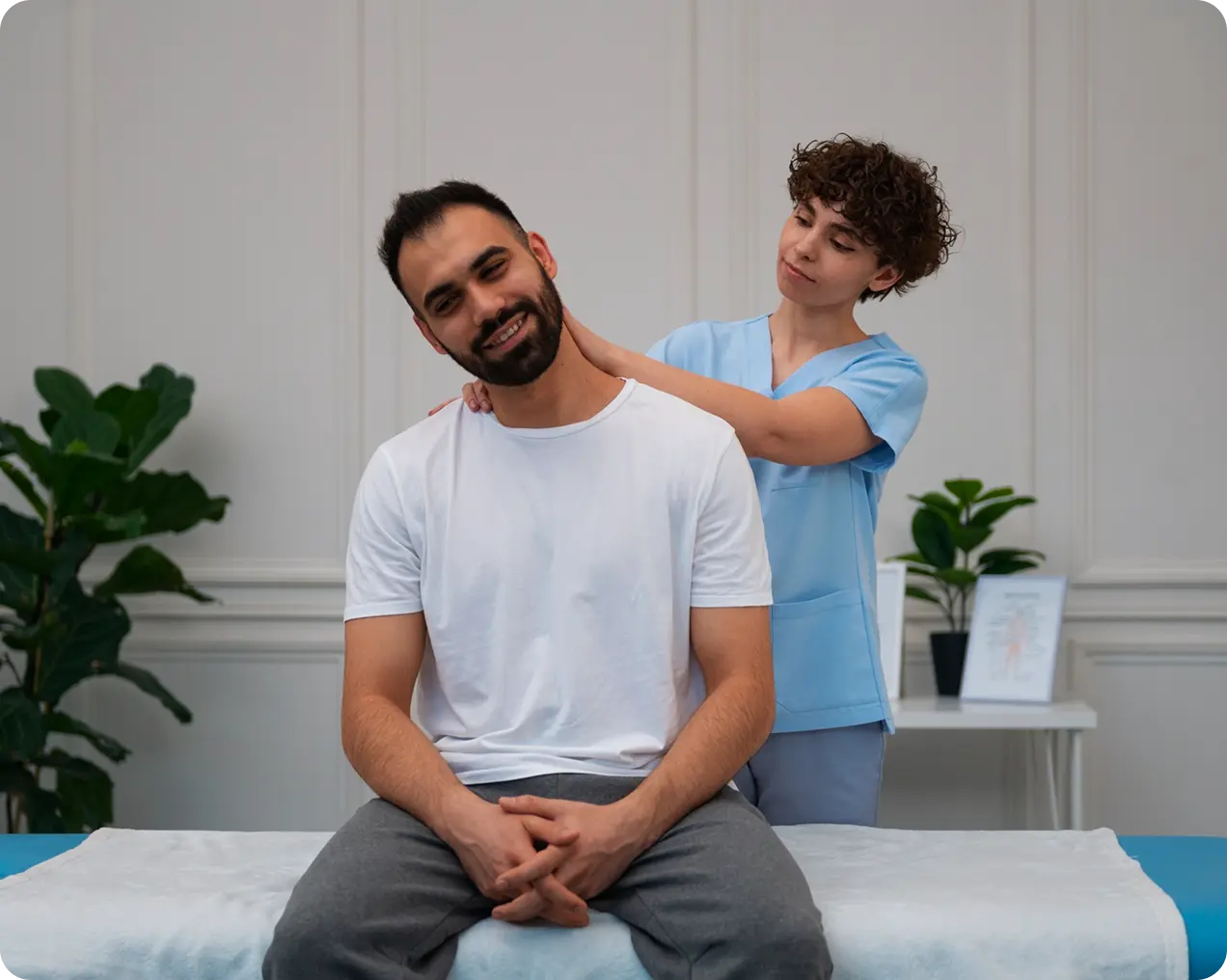 A physical therapist in blue scrubs gently stretches a man's neck with him seated on a treatment table.