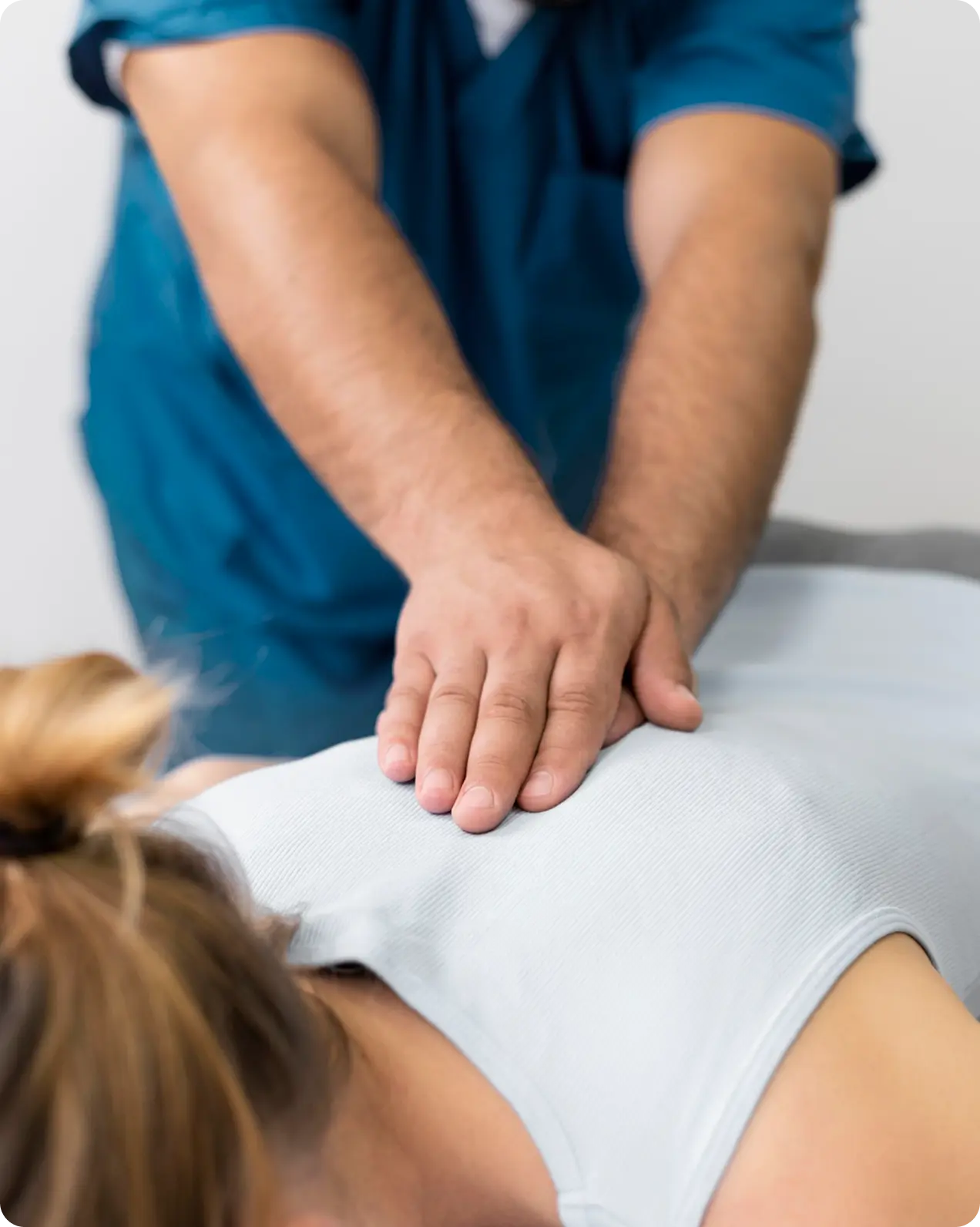 Therapist wearing blue uniform giving a back massage to a woman lying face down.