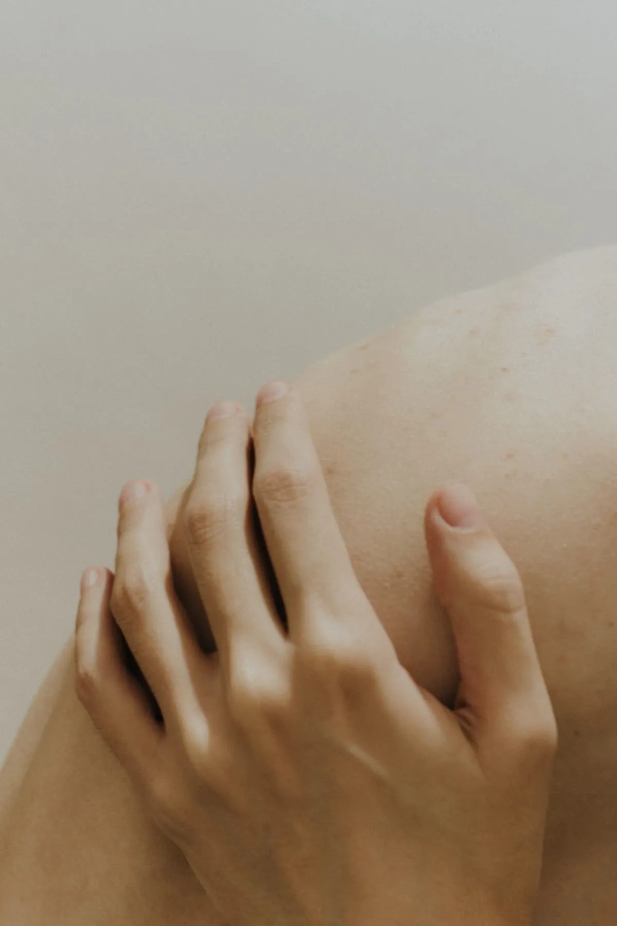 Close-up of a hand gently resting on a bare shoulder against a plain background.