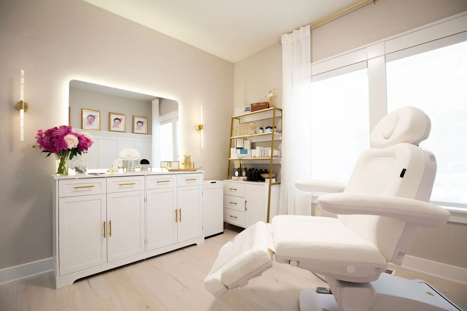 Bright modern treatment room with white recliner chair and cabinet with flowers and skincare products.