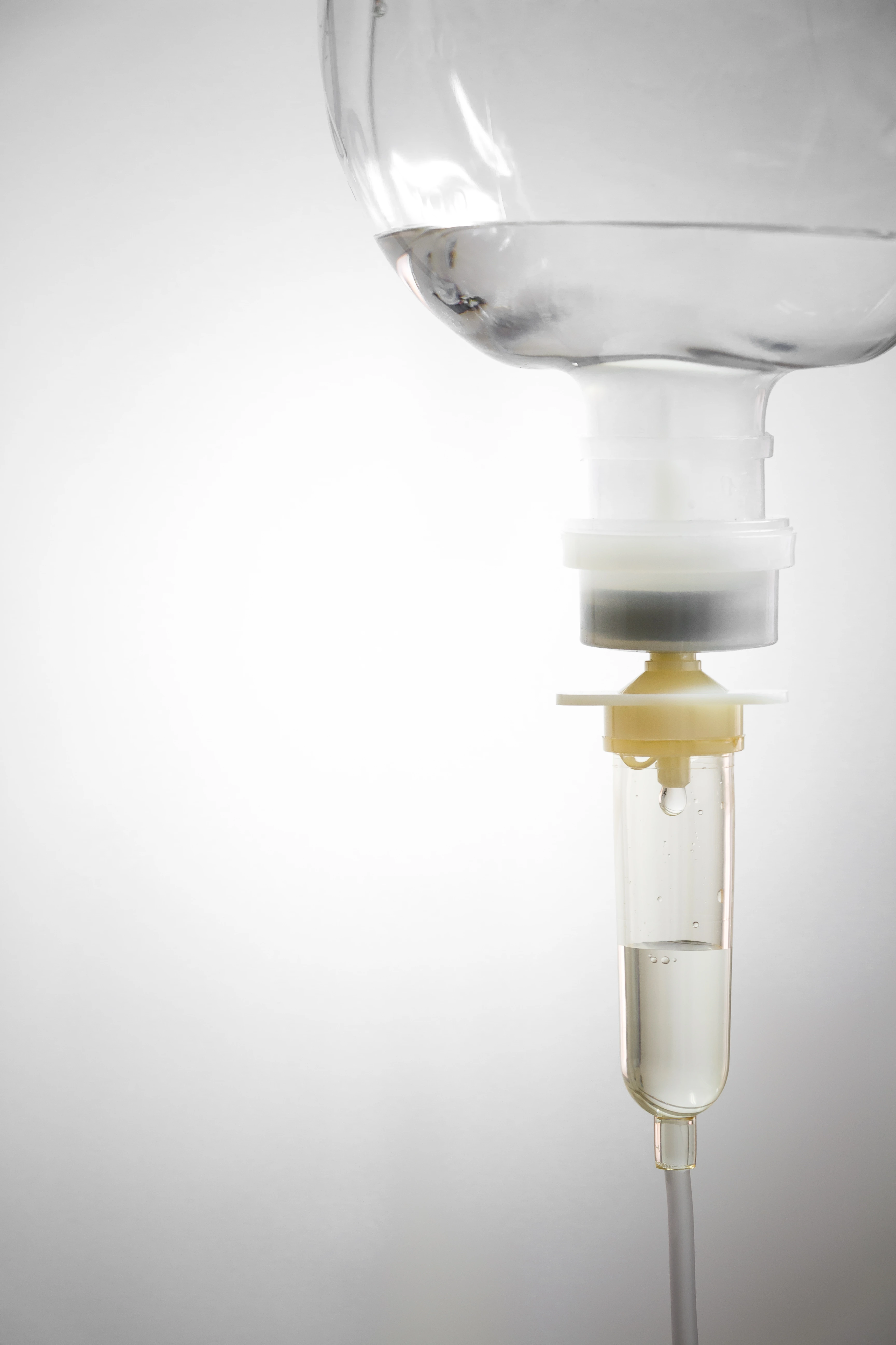 Close-up of a saline IV drip chamber with a drop of fluid ready to fall.