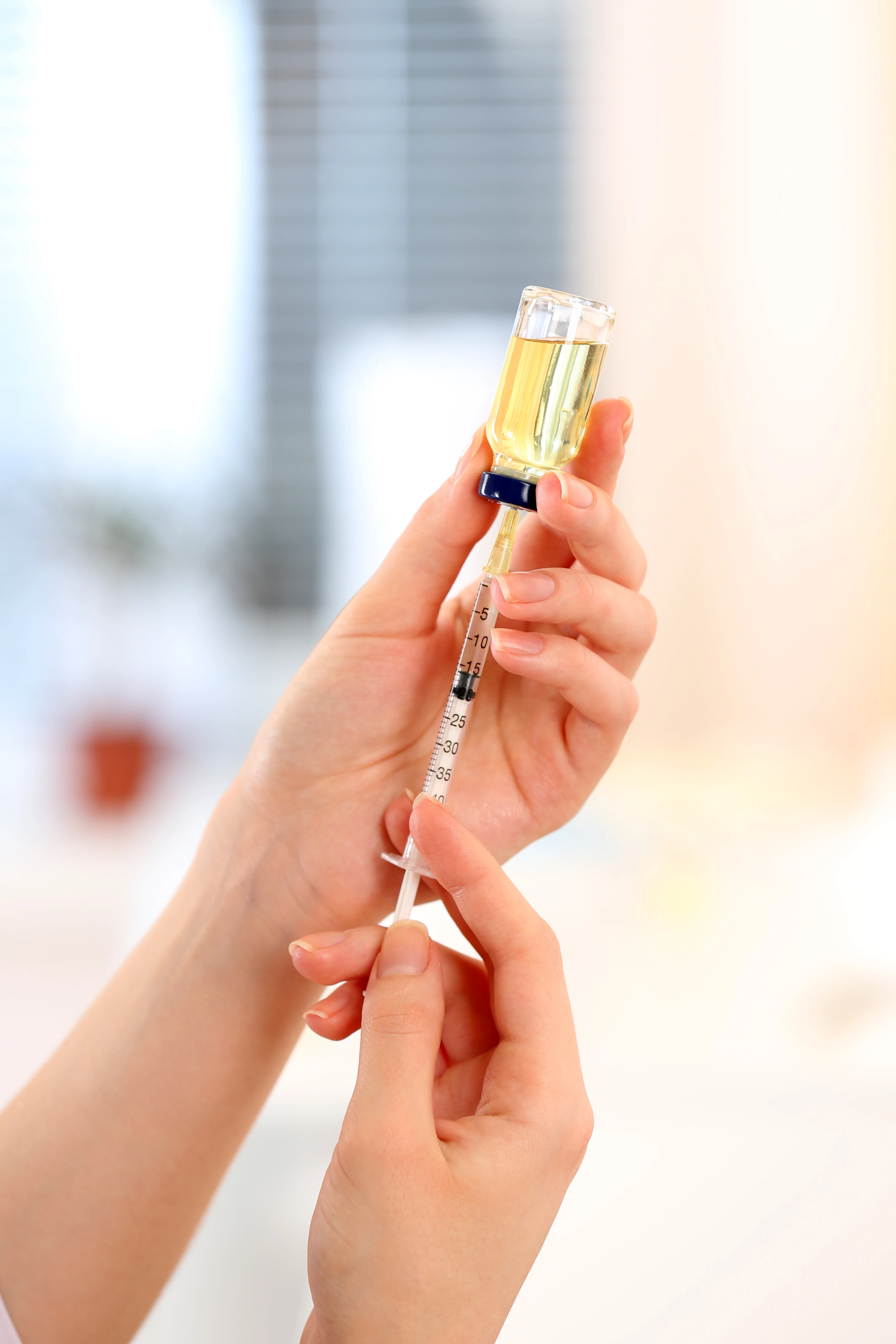 Hands holding a syringe and a vial with yellow liquid being drawn into the syringe.