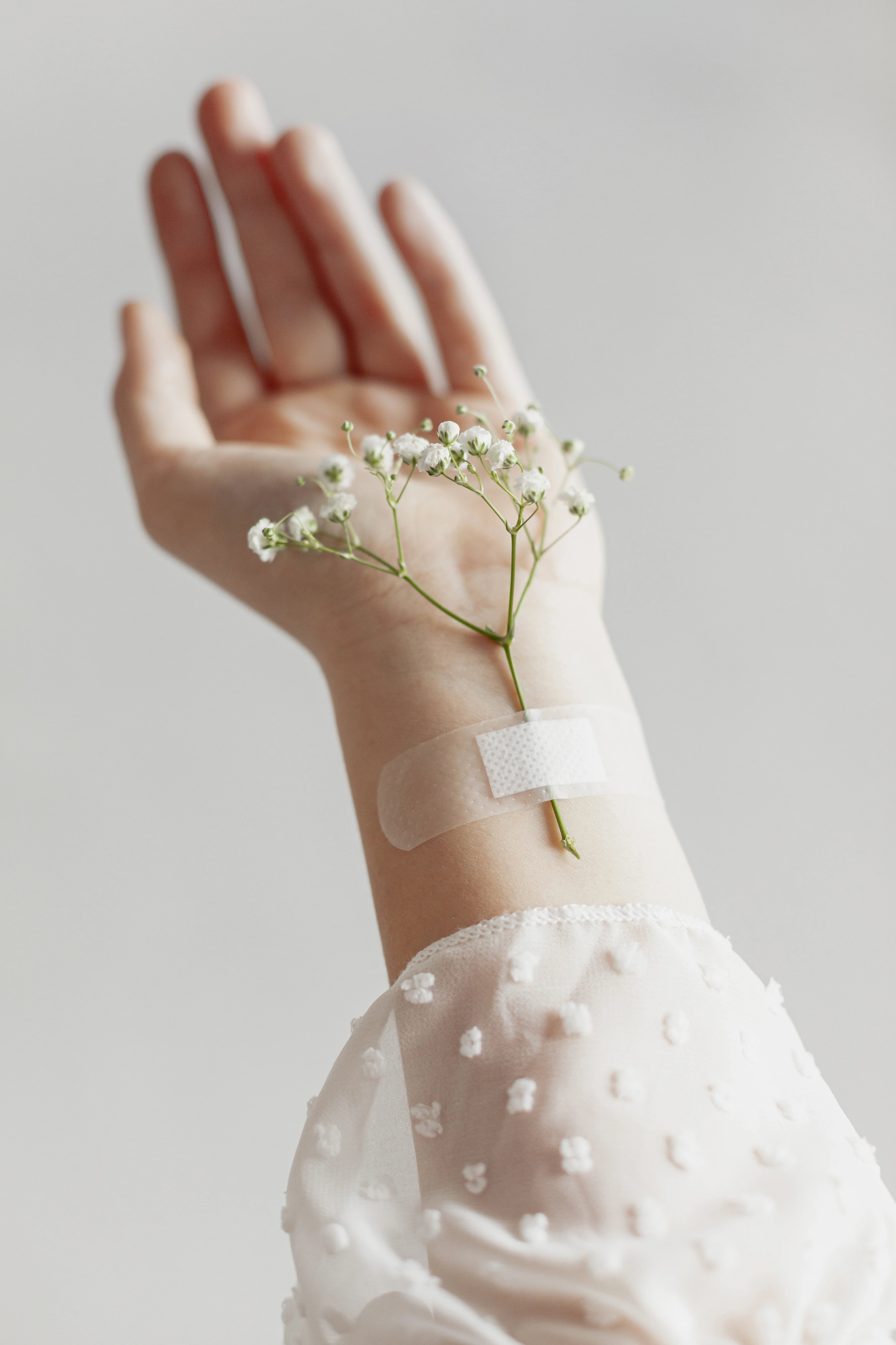 Delicate white flowers taped to the wrist of a hand with sheer white dotted fabric sleeve.