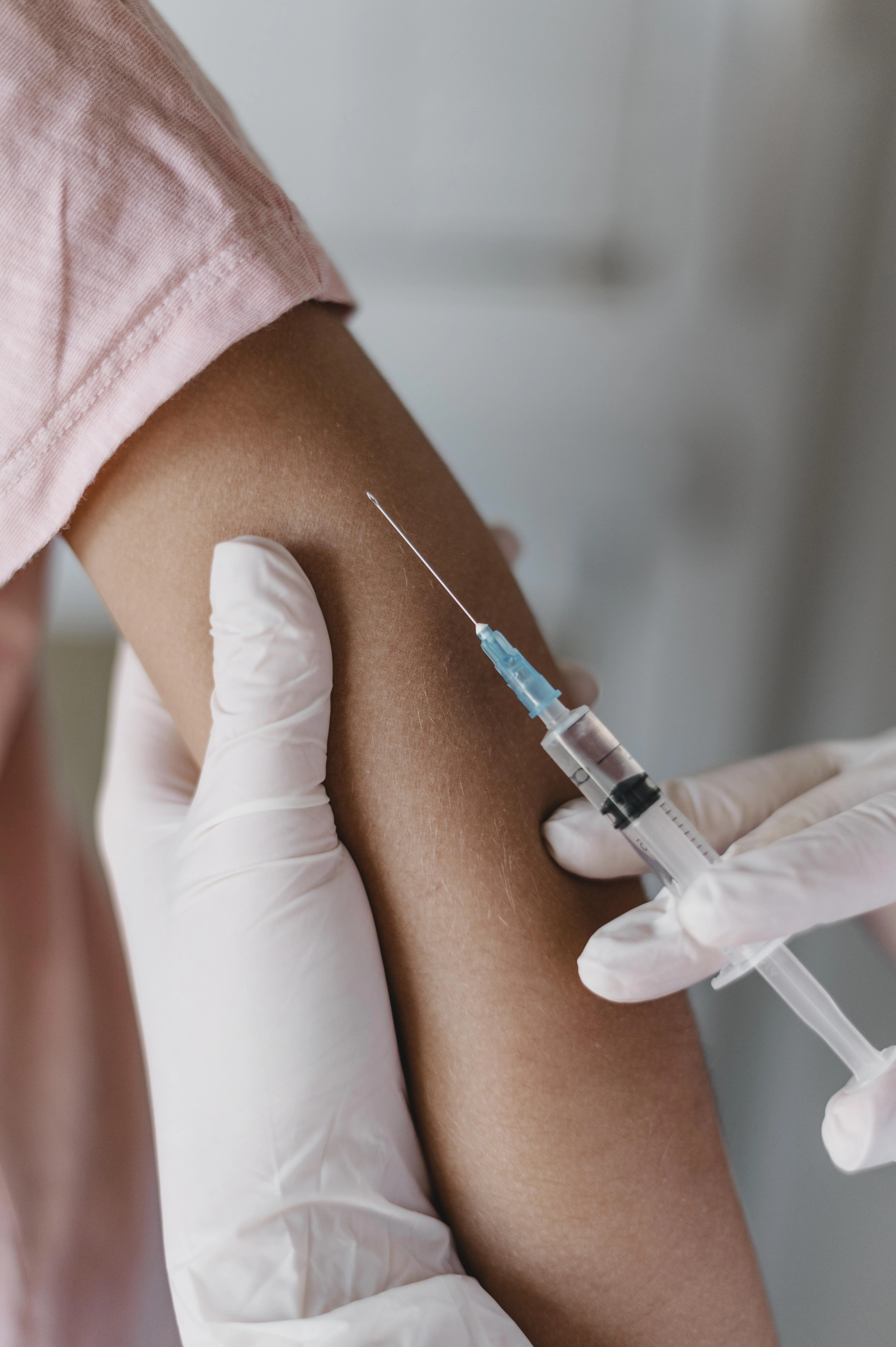 Close-up of a gloved hand giving a vaccine injection to a child's upper arm.