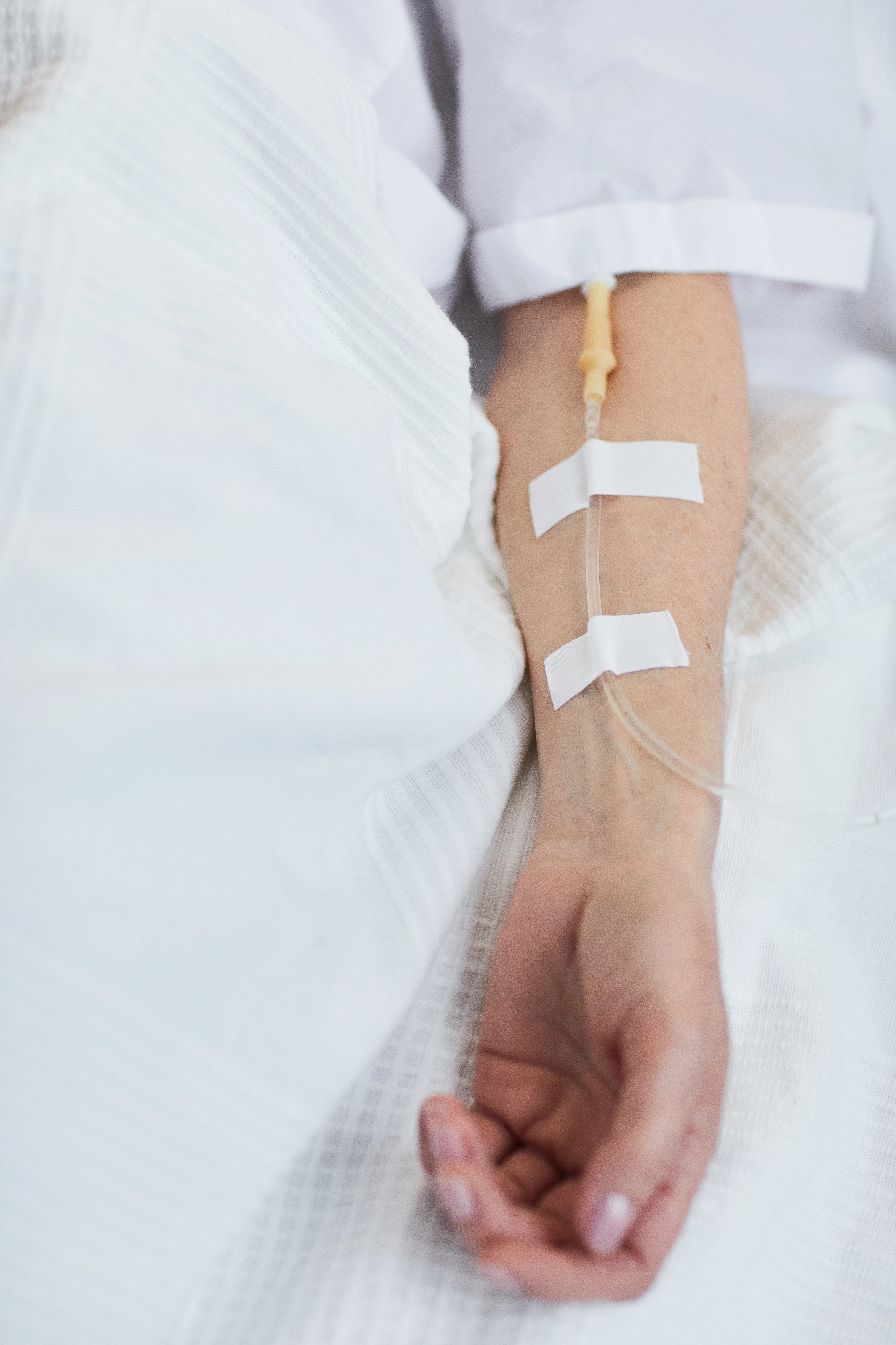 Close-up of a patient's arm with an intravenous drip taped in place while lying in a hospital bed.