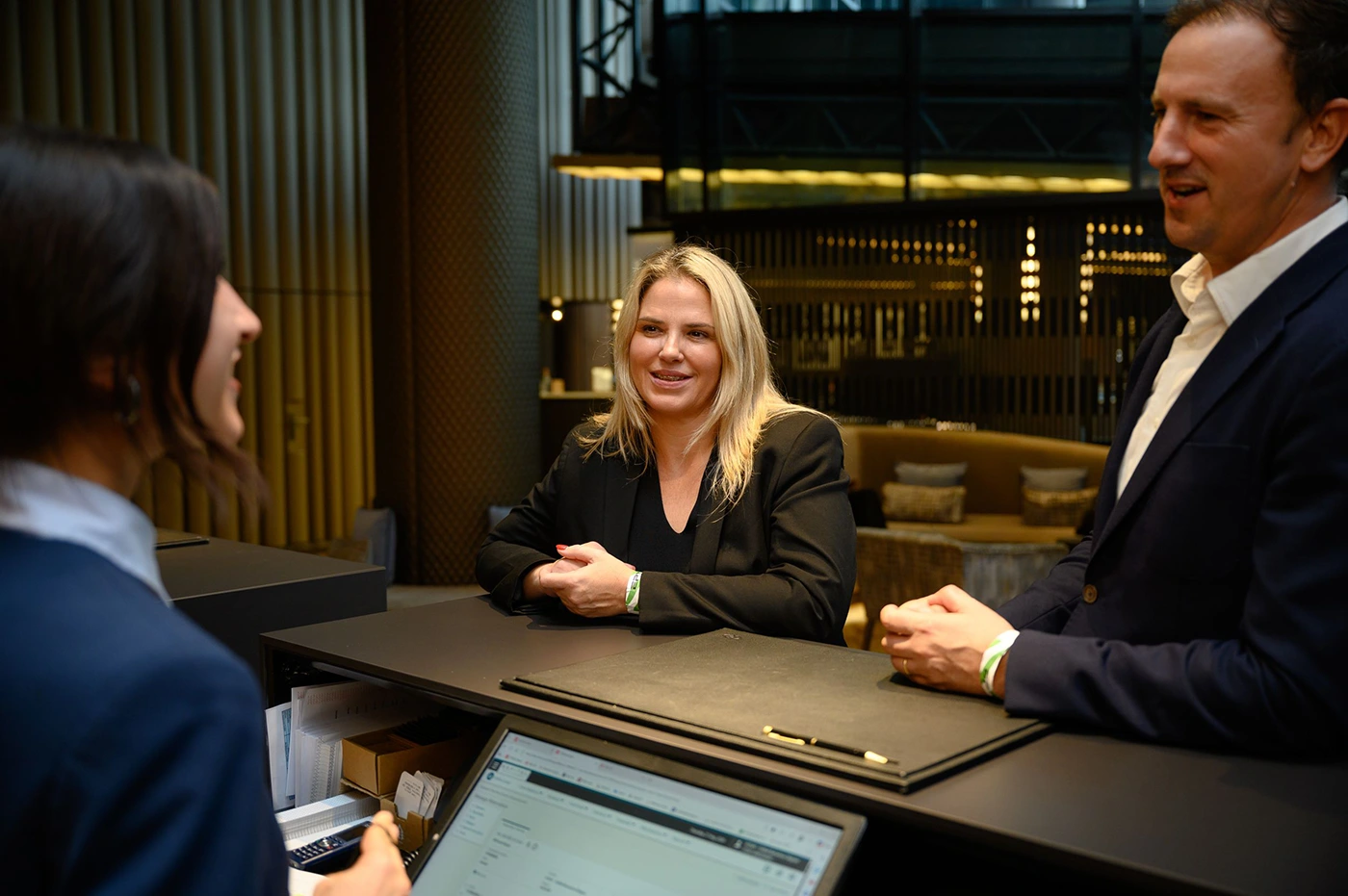A man and a woman talking nicely to a woman at a the front desk of a hotel.
