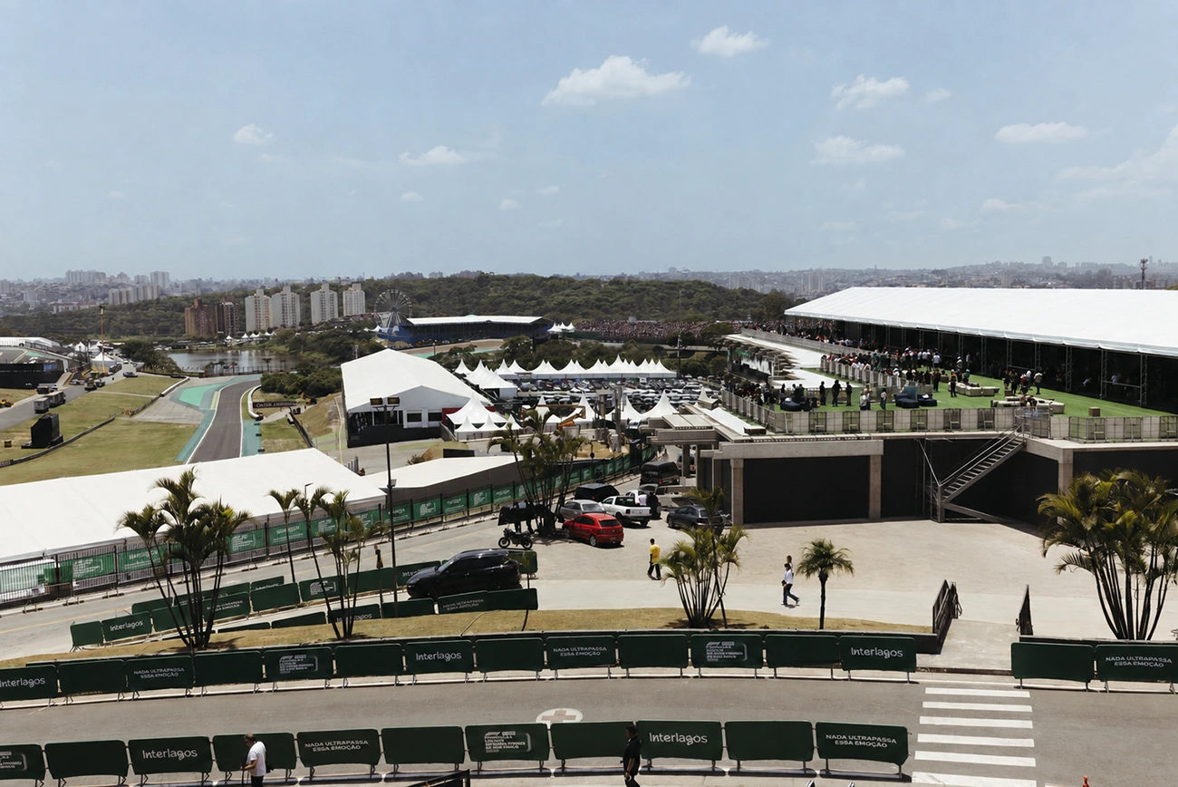 Aerial view of Wide aerial view of a motorsport event venue with race track, grandstands filled with spectators, tents, palm trees, parked cars, and people walking around under a clear sky.a racing circuit.
