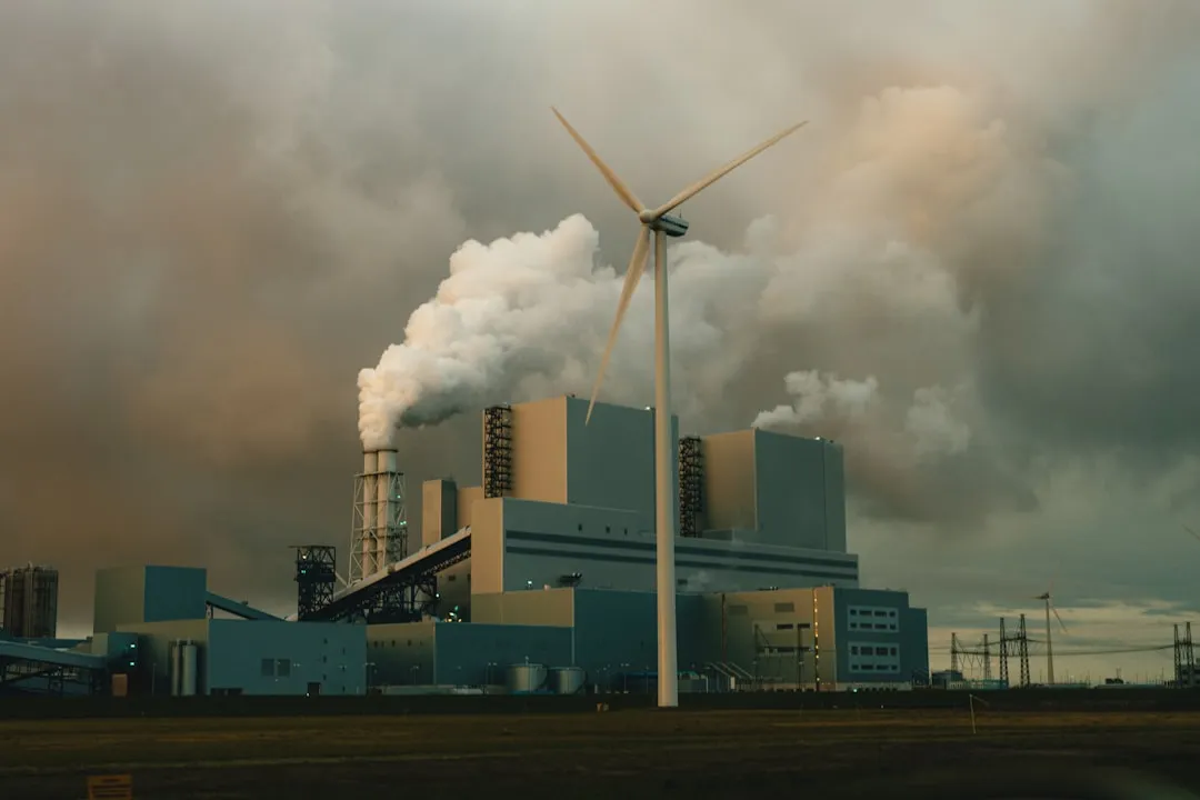 a factory with smoke billowing out of it's stacks. Photo by Tim van der Kuip on Unsplash