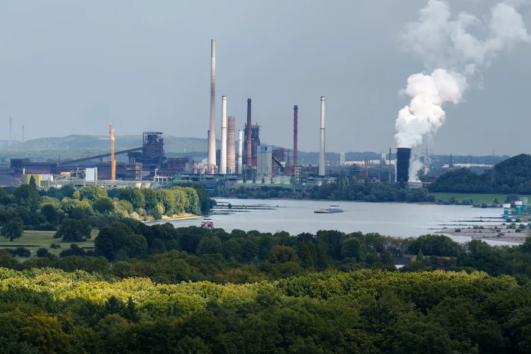 Industrial complex with smokestacks near a body of water.. Photo by Jakub Żerdzicki on Unsplash
