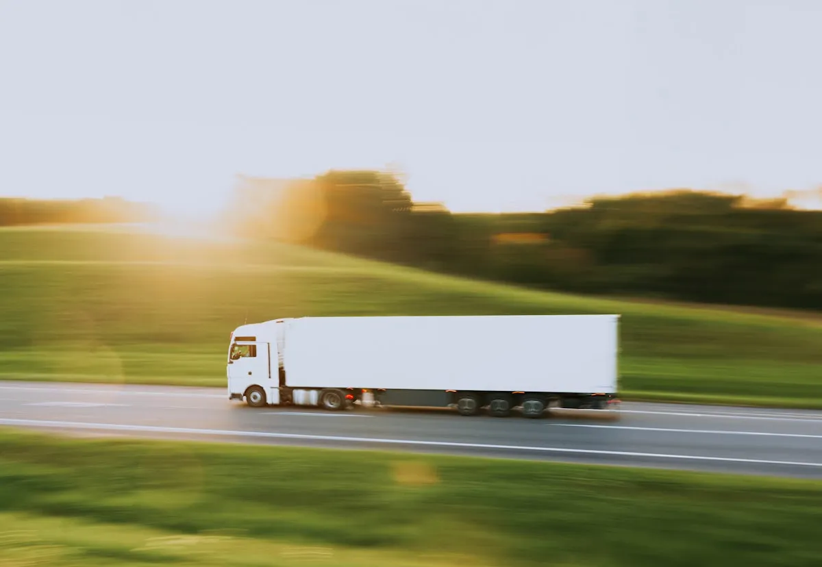 a white semi truck driving down a rural road. Photo by Artem Balashevsky on Unsplash