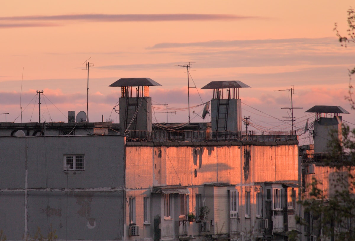 Rooftops with chimneys against a soft sunset sky — Photo by Evgenii Dzhivelikian on Unsplash