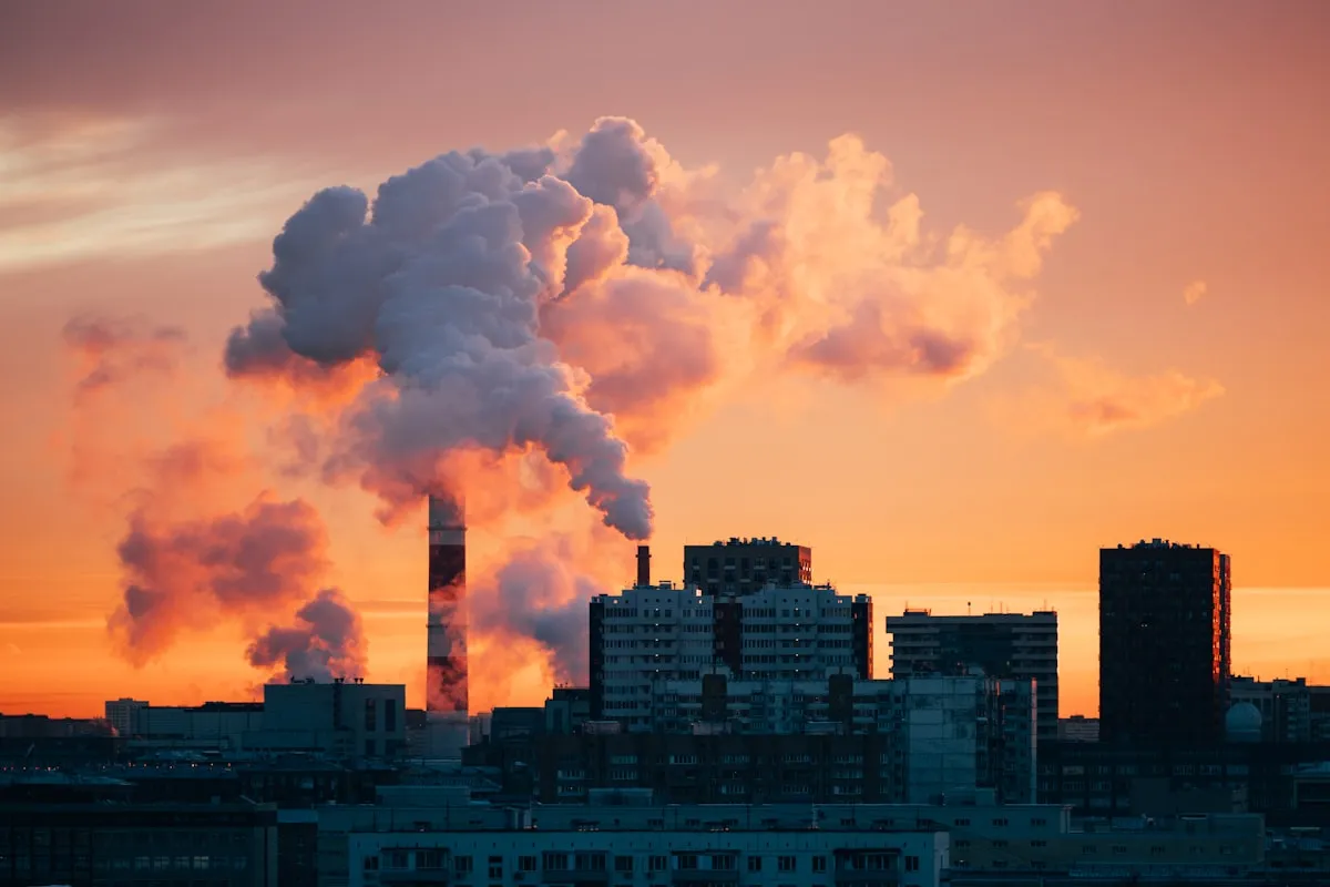 Factory smokestacks emitting smoke against sunset sky., Photo by ROMAN Z. on Unsplash