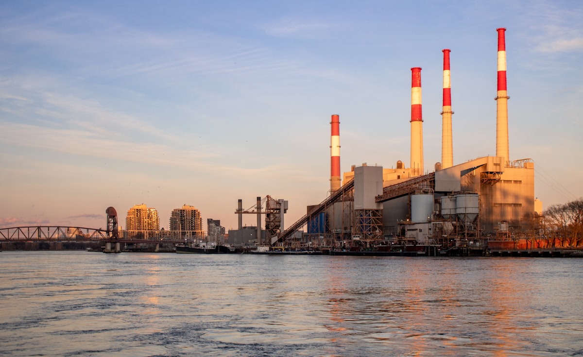 A power plant stands near water under a blue sky., Photo by Zoshua Colah on Unsplash