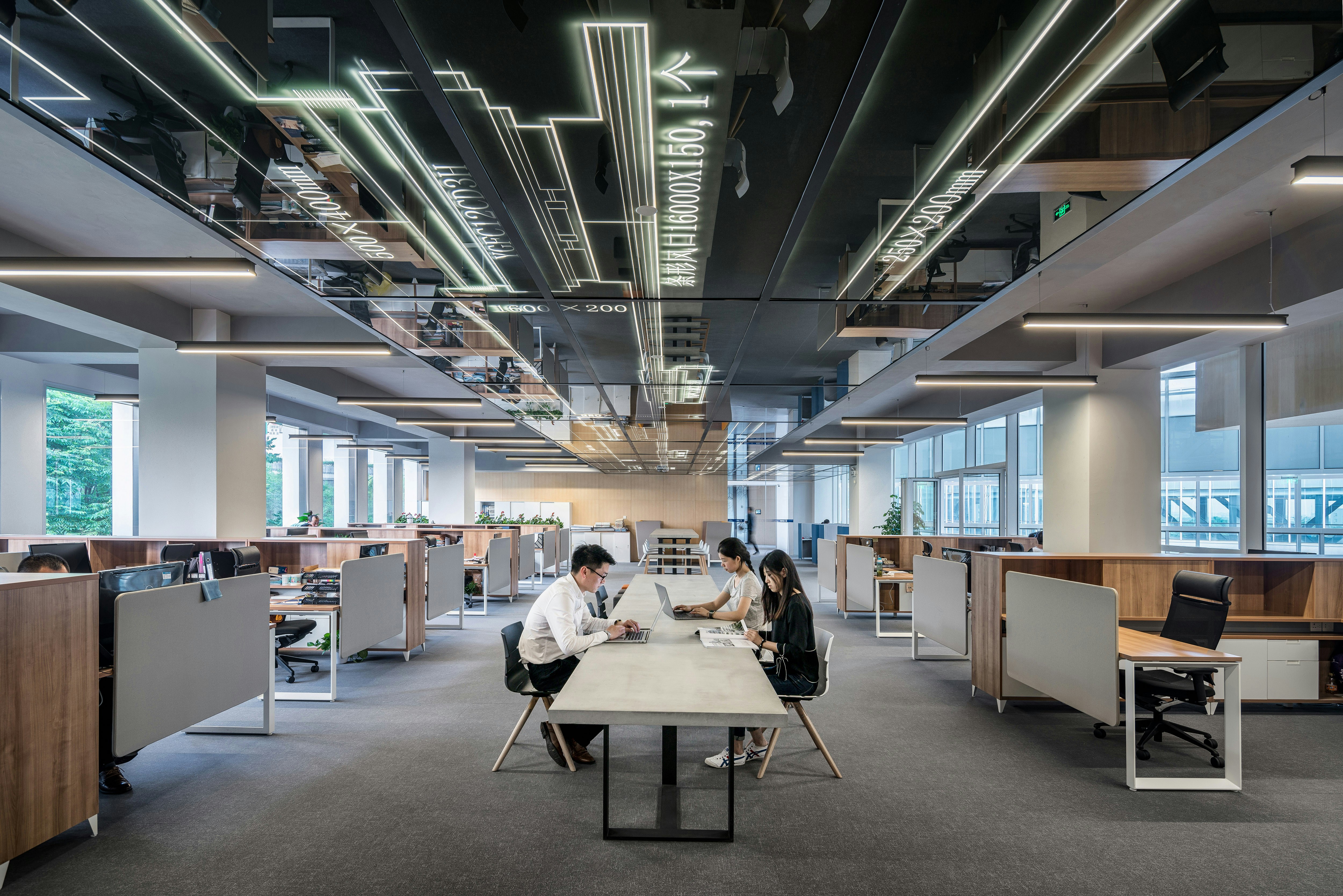 Open-plan office with long rows of desks and people working at a shared table