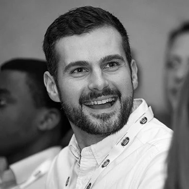 Ben Thornton-Jones, smiling, bearded, in black and white, wearing a white shirt